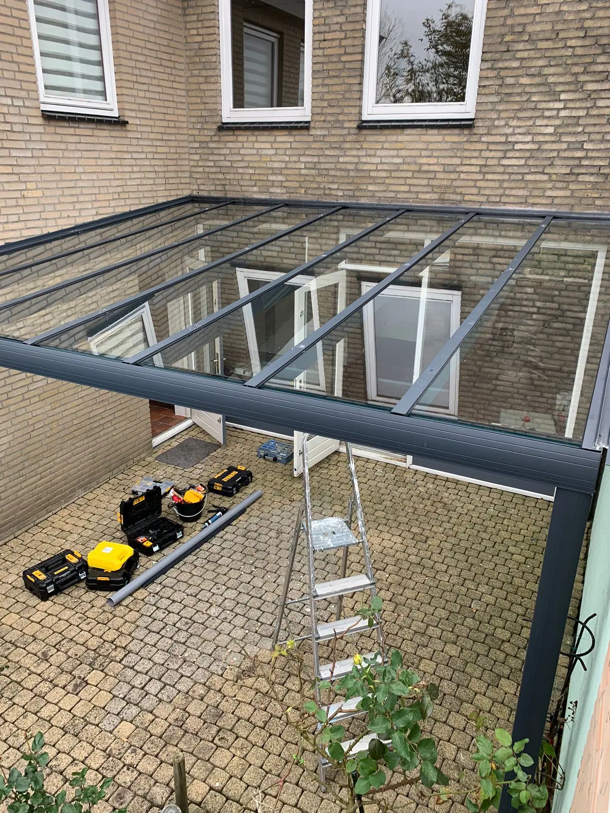A glass roof seen from above, with tool cases and a ladder on the paving below it