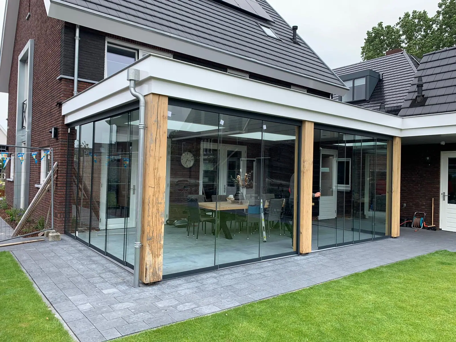 Garden room against the house with oak posts and glass sliding walls on two sides