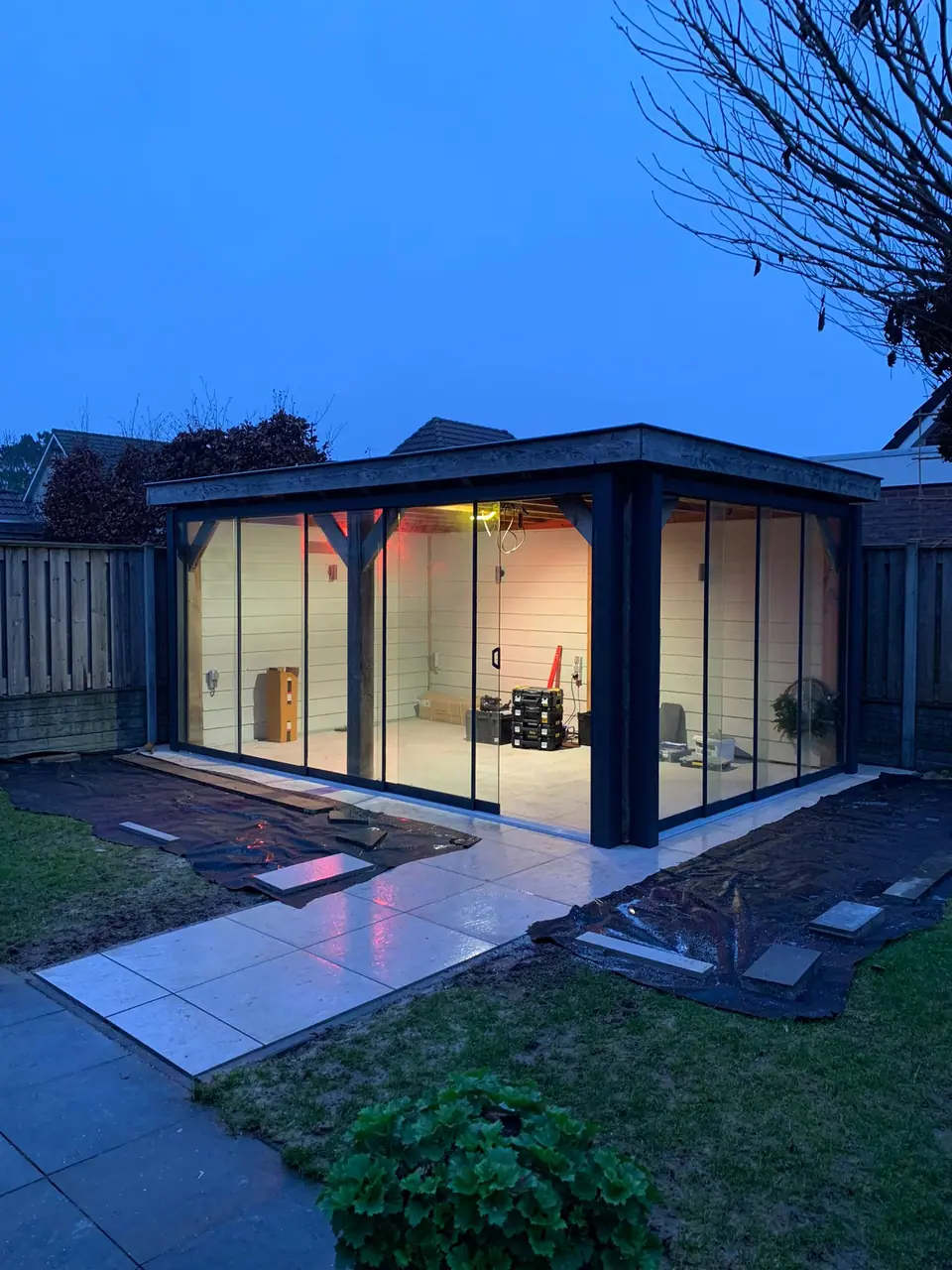 Free-standing garden room with glass sliding walls, lit from within at dusk